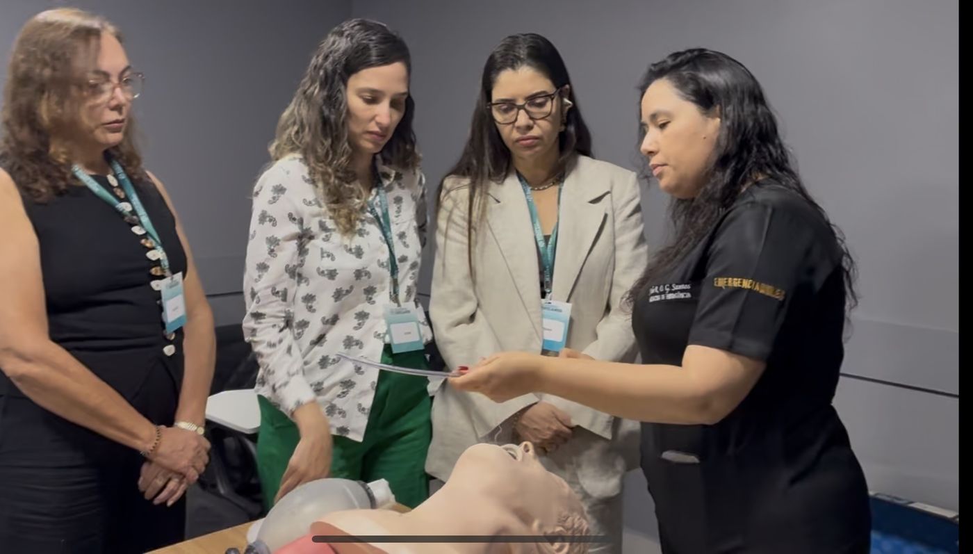 Instrutora demonstrando bougie para alunas em torno do manequim de via aérea